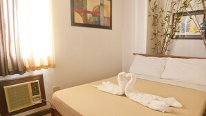 A neatly made bed with white towels folded into swans, a bedside table with a radio, and a window with sheer curtains. - Isabelle Garden Hotel and Suites (Parañaque)