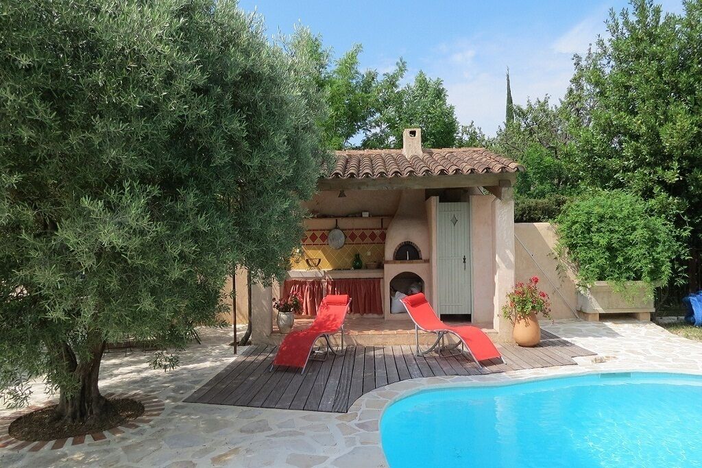 A poolside area with a tiled deck, a small building with a tiled roof, and a tree.