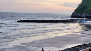 Una playa con un rompeolas rocoso, aguas tranquilas y un barco anclado cerca de la orilla.