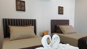 Habitación de hotel con dos camas, cada una con cabecero marrón y ropa de cama color crema. Hay almohadones decorativos y una pequeña figurina naranja en la mesita de noche.