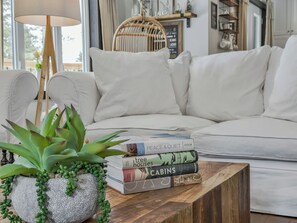 Una sala de estar con un sofá blanco, una mesa de centro de madera con libros y una planta en maceta.
