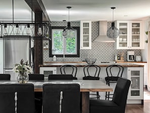 Una cocina moderna con comedor, que incluye una mesa de madera, sillas negras y luces colgantes.