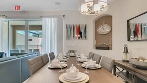 Un coin repas avec une longue table dressée pour le repas, une horloge au mur et une vue sur l’extérieur.