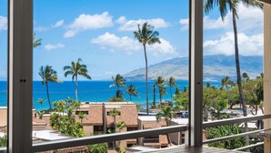Un balcon avec vue sur l’océan, les palmiers et les bâtiments.
