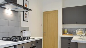 Cocina moderna con estufa a gas, horno y cafetera. Se observa una puerta de madera y armarios grises.