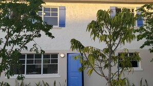 A two-story building with a blue door, white windows, and a small garden area with various plants.