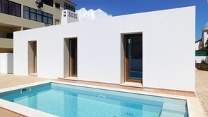A swimming pool adjacent to a white building with three doors and windows. - Brand New Villa with Private Pool and Lovely Garden near the beach.
 (Alvor)