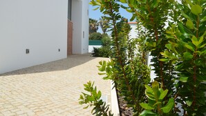 A paved courtyard with a white building, a brick section, and green foliage. - Brand New Villa with Private Pool and Lovely Garden near the beach.
 (Alvor)