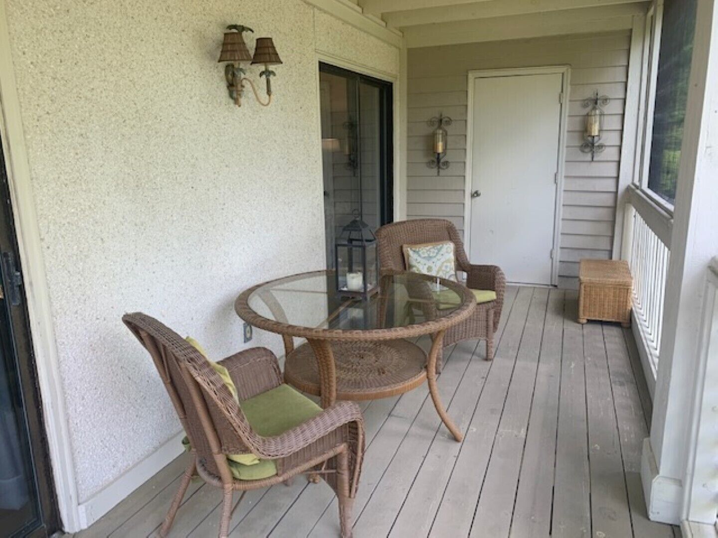 Eine überdachte Veranda mit Korbmöbeln und einem Glastisch.