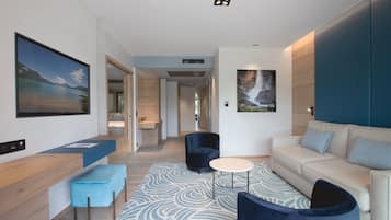 A modern hotel room with a large window, a sofa, a coffee table, and a blue accent chair.