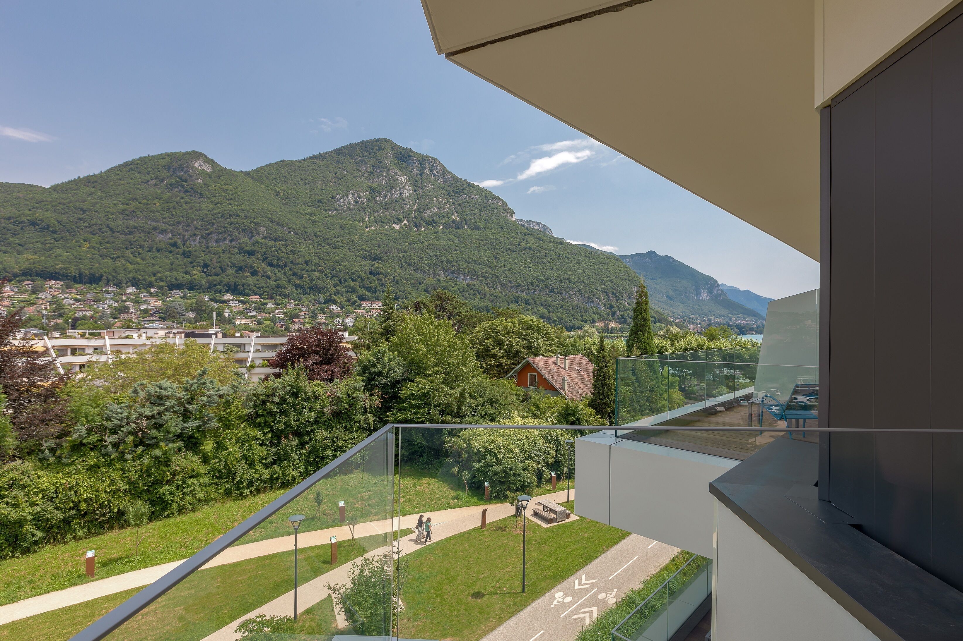 A balcony with a view of a mountainous landscape, a paved path, and a small red house.