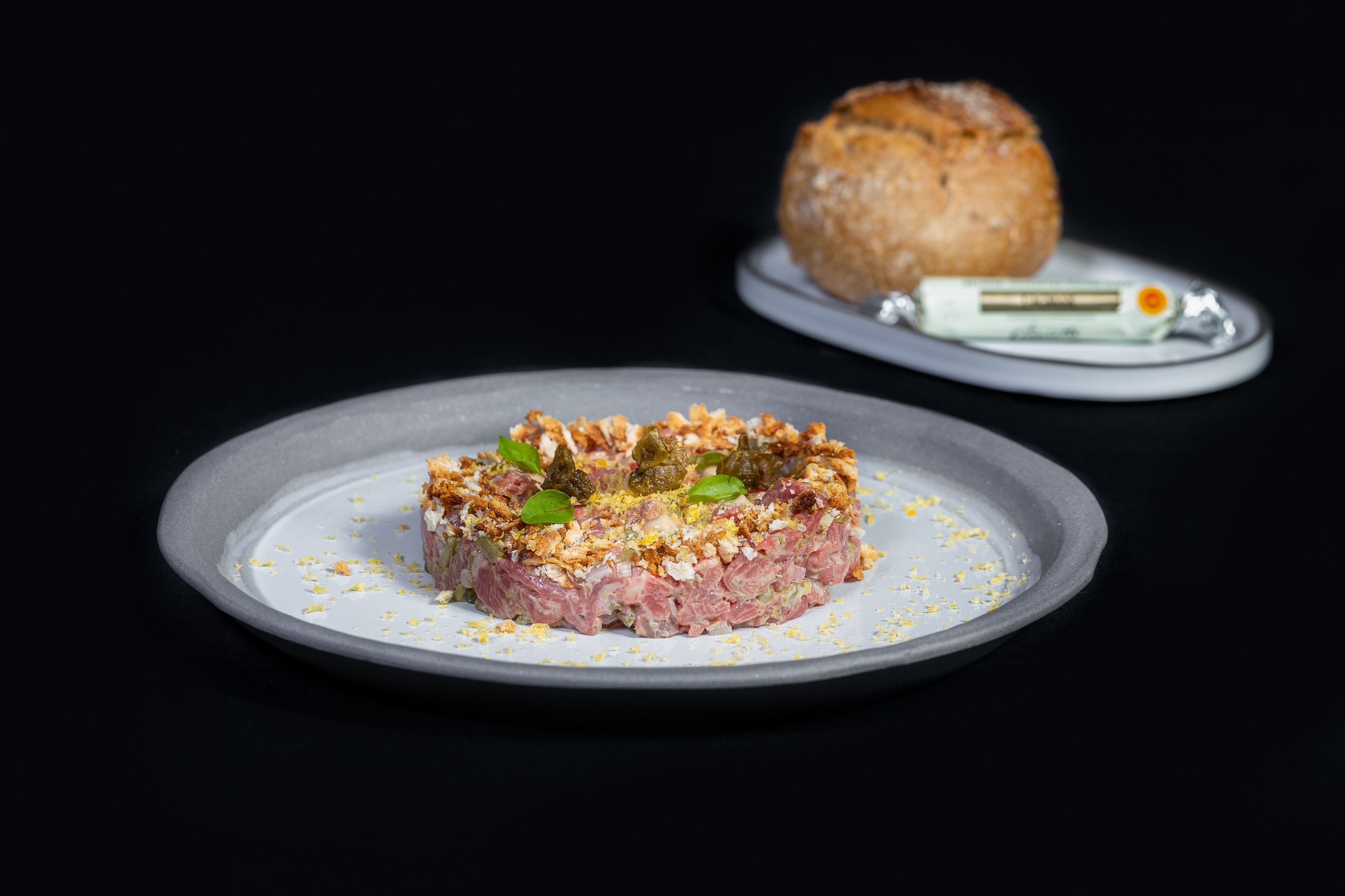 A slice of meat terrine on a plate with a side of bread and a small container of butter.