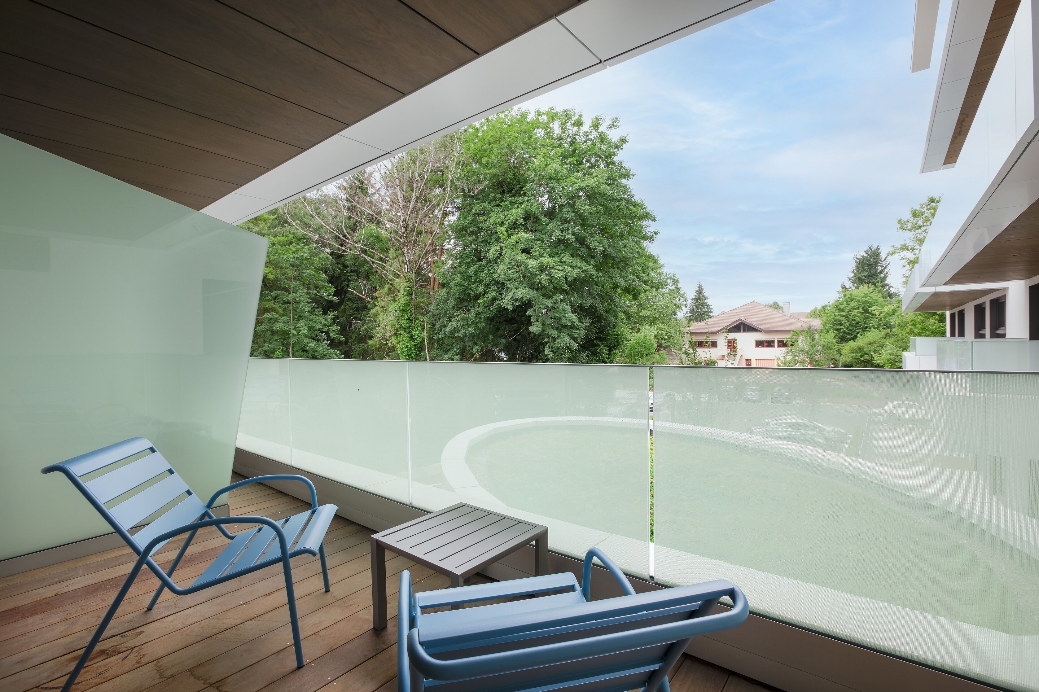 Un balcon avec deux chaises bleues et une petite table, donnant sur une piscine et un bâtiment doté d’un toit en pente.
