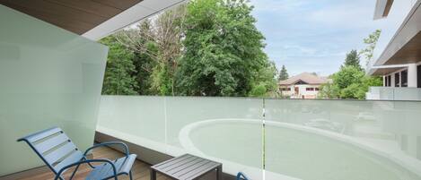 Un balcon avec deux chaises bleues et une petite table, donnant sur une piscine et un bâtiment doté d’un toit en pente.