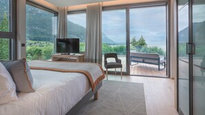 Une chambre dotée d’un grand lit, d’une télévision et offrant une vue sur un paysage montagneux grâce à de grandes fenêtres.