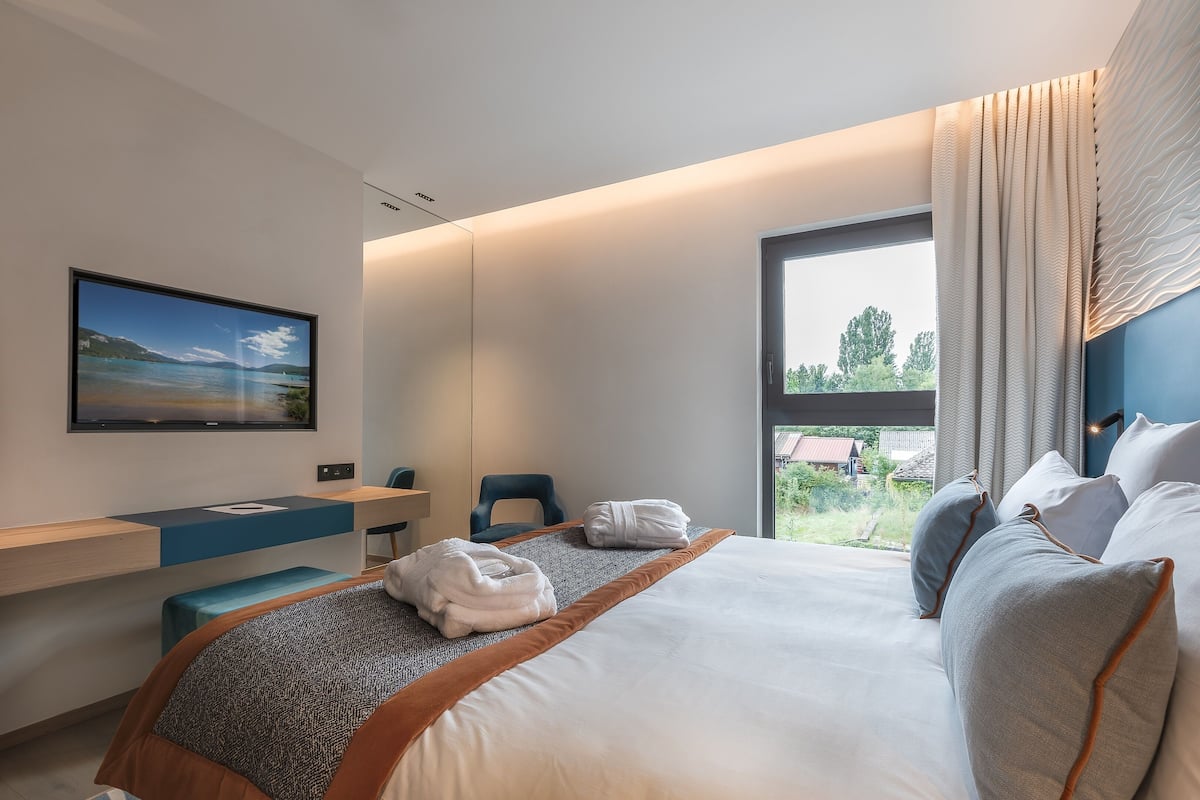 A modern hotel room with a bed, a desk, and a large window.