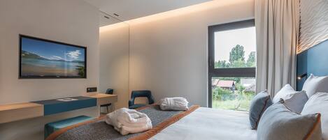 A modern hotel room with a bed, a desk, and a large window.