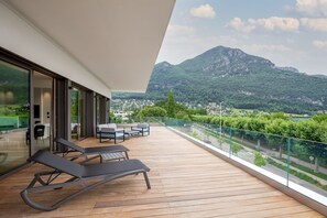 A balcony with wooden flooring and two lounge chairs, overlooking a mountainous landscape with a clear sky.