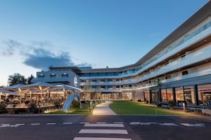 A modern hotel with a curved facade, outdoor seating area, and a well-lit entrance.