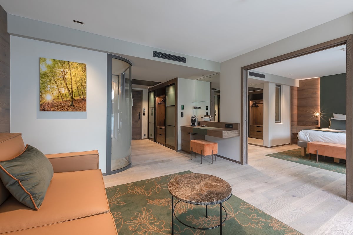A modern hotel room with a sofa, a round table, a bed, a bathroom, and a kitchen area.