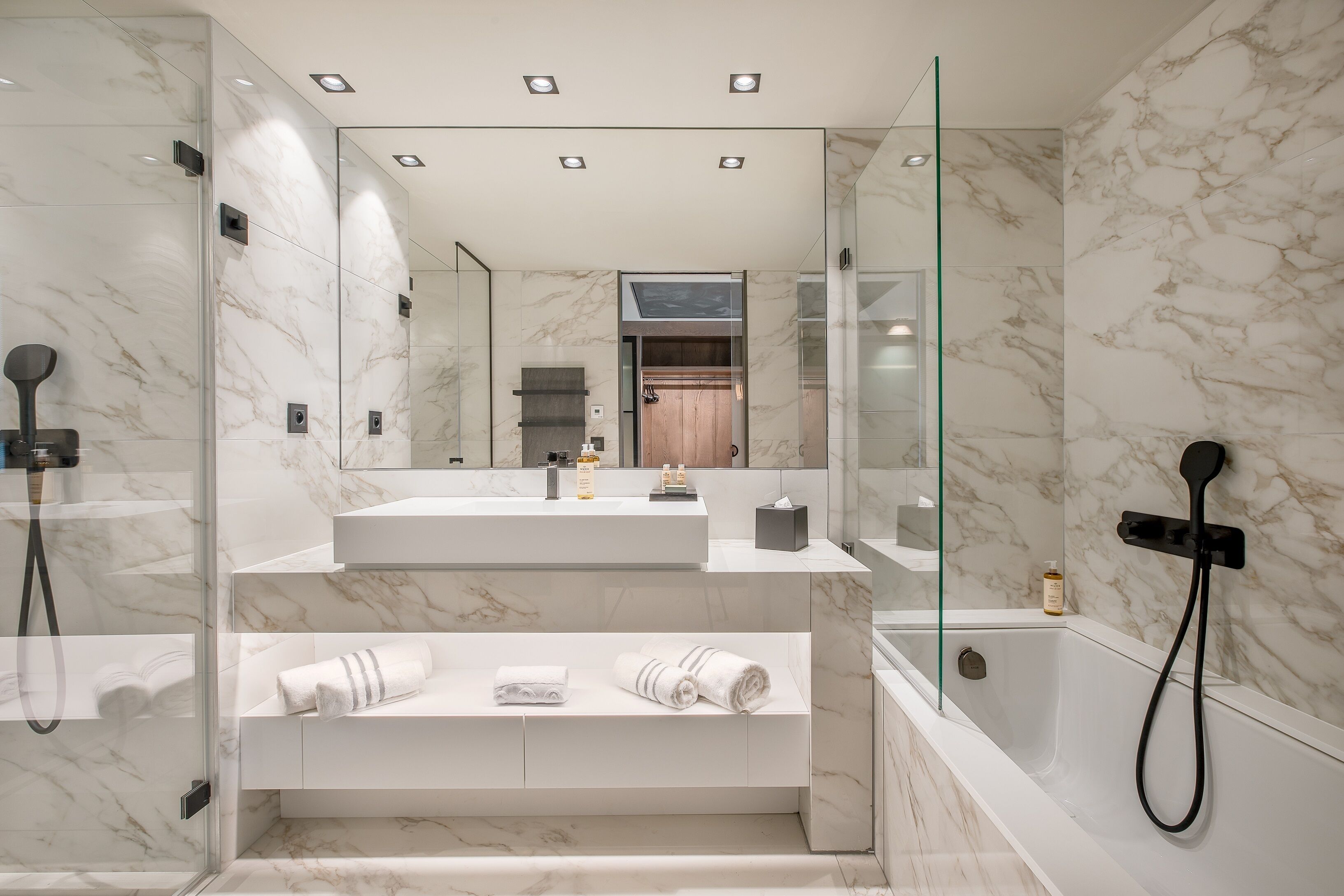 Une salle de bain moderne avec un mur en marbre, une douche en verre, un lavabo intégré et un meuble-lavabo avec des serviettes.