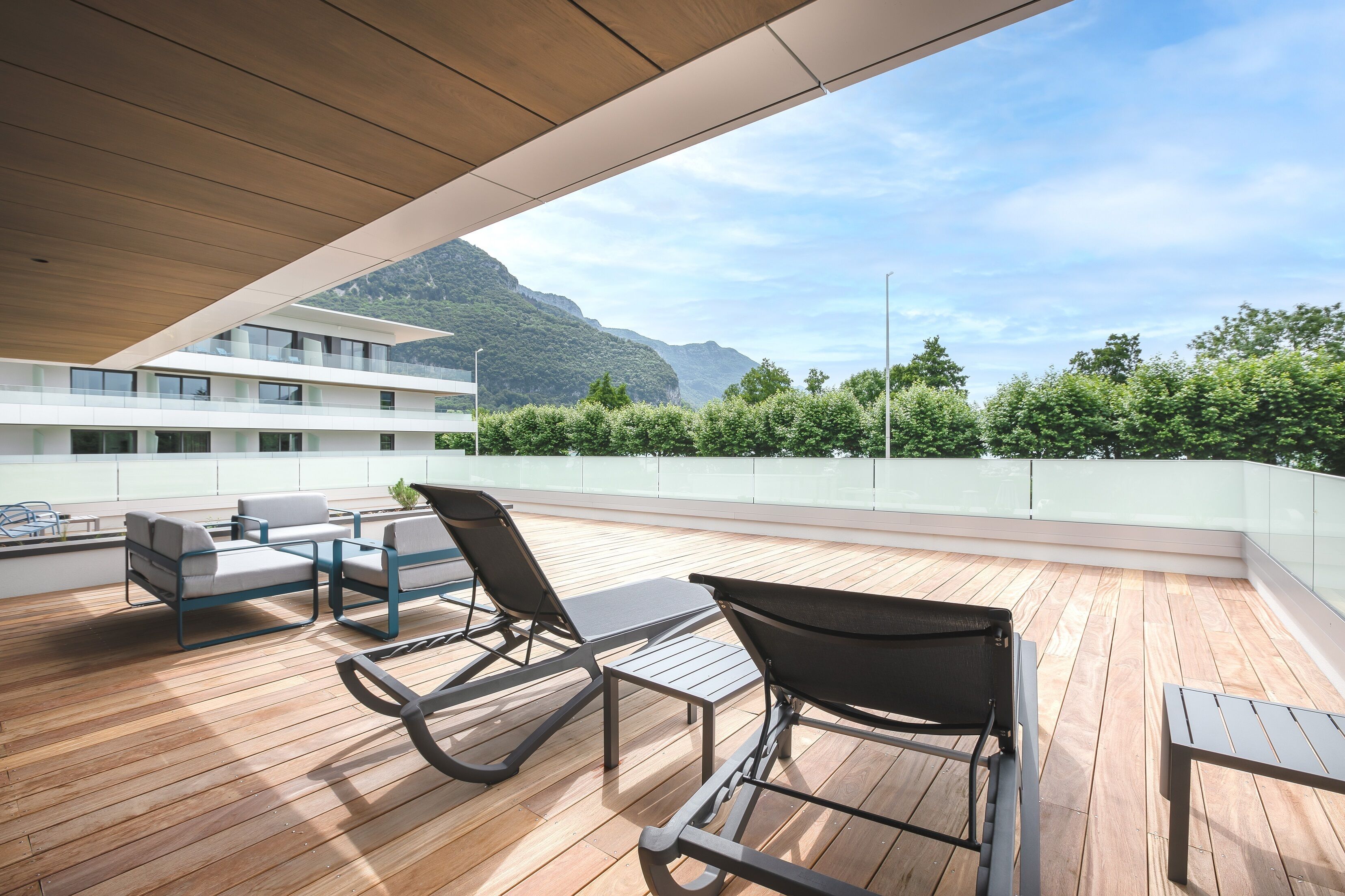 A wooden deck with outdoor furniture, a view of mountains, and a building in the background.