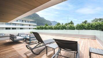 A wooden deck with outdoor furniture, a view of mountains, and a building in the background.