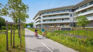 Een pad met twee fietsers, een modern gebouw met meerdere verdiepingen en een gazon met bomen.