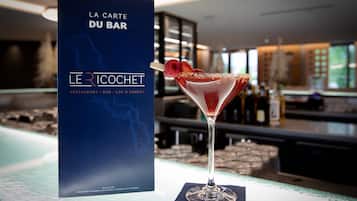 Ein Cocktailglas mit Erdbeere als Dekoration auf einer Bartheke, im Hintergrund eine Speisekarte mit der Aufschrift "LA CARTE DU BAR".