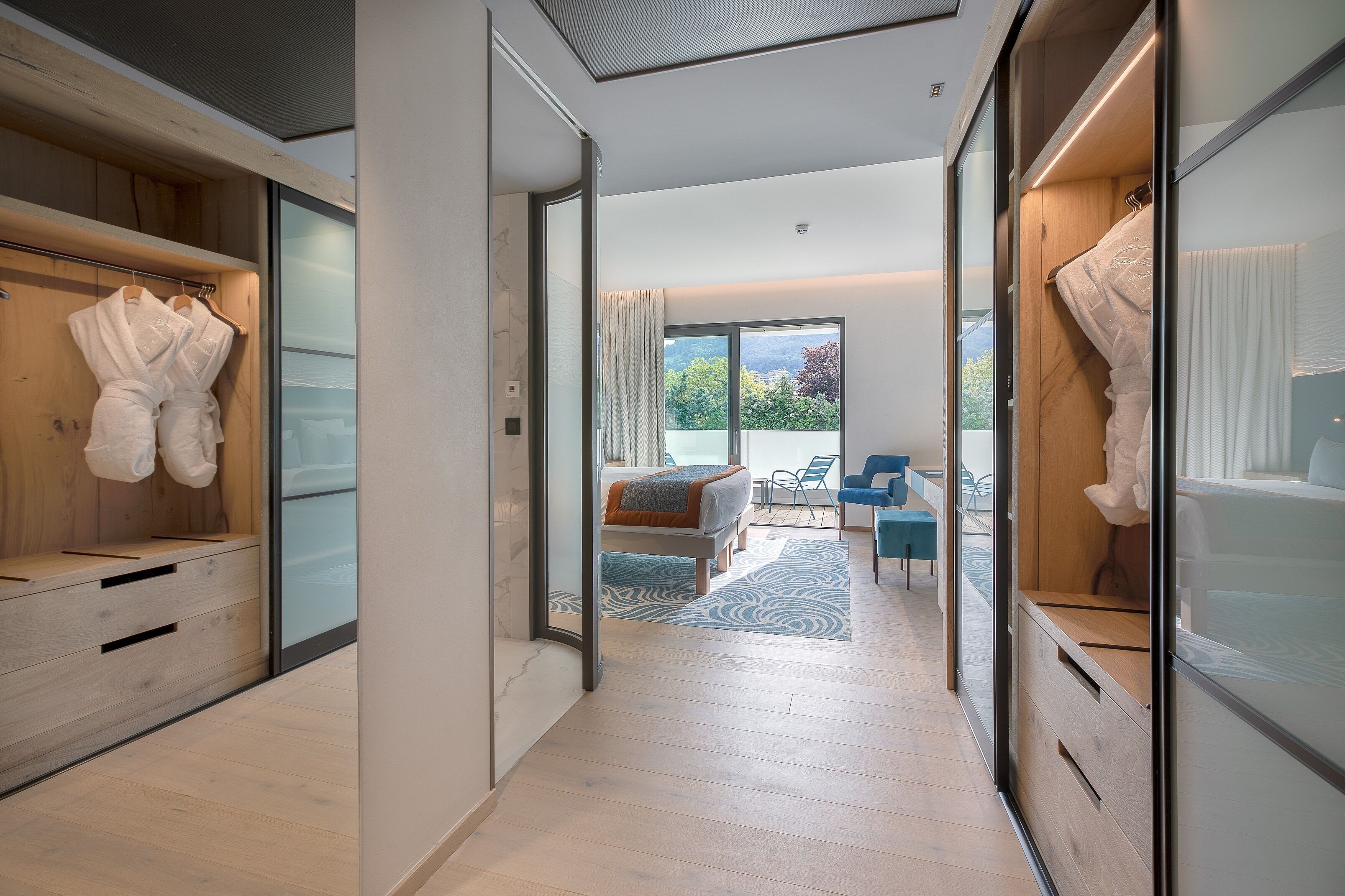 A modern hotel room with a wooden wardrobe, a bed with a view, and a seating area with a view.