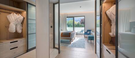 A modern hotel room with a wooden wardrobe, a bed with a view, and a seating area with a view.