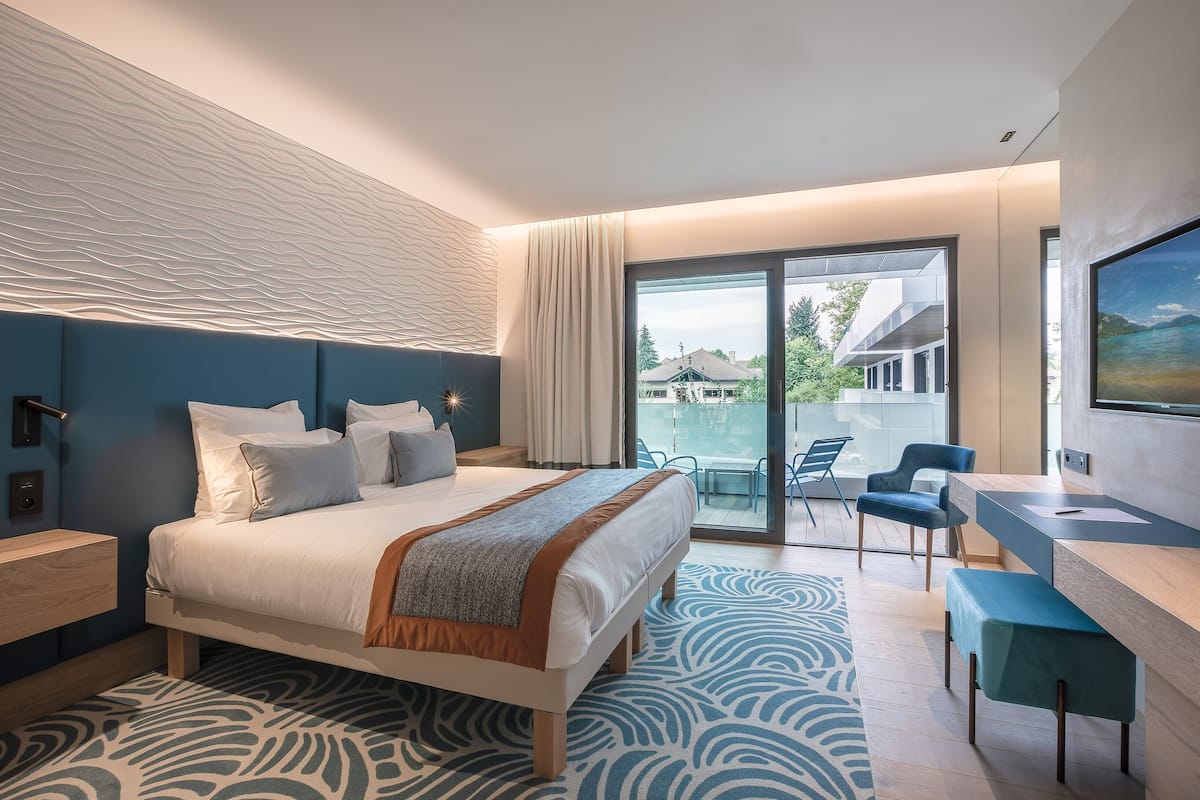 A modern hotel room with a large bed, a desk, and a view of the outside.