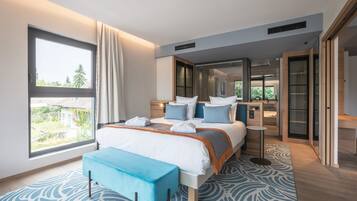 A modern hotel room with a large bed, a view through a window, a bedside table, and a bench.