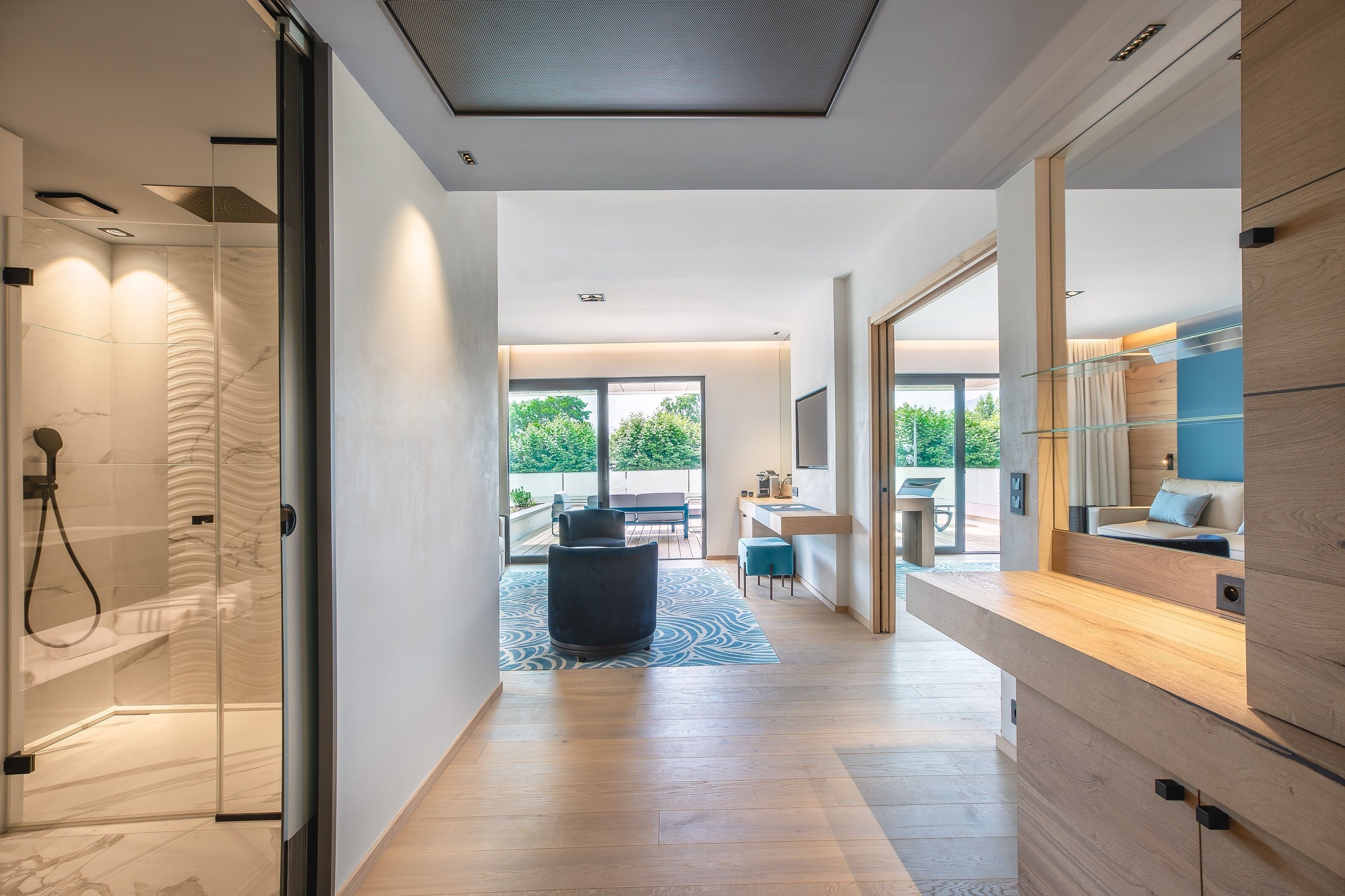A modern hotel room with a glass shower, a wooden vanity, a large window, and a view of the outdoors.