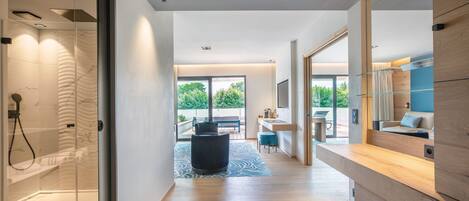 A modern hotel room with a glass shower, a wooden vanity, a large window, and a view of the outdoors.