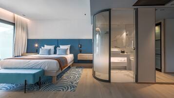 A modern bedroom with a bed, a bench, a glass-enclosed walk-in closet, and a bathroom with a marble floor.