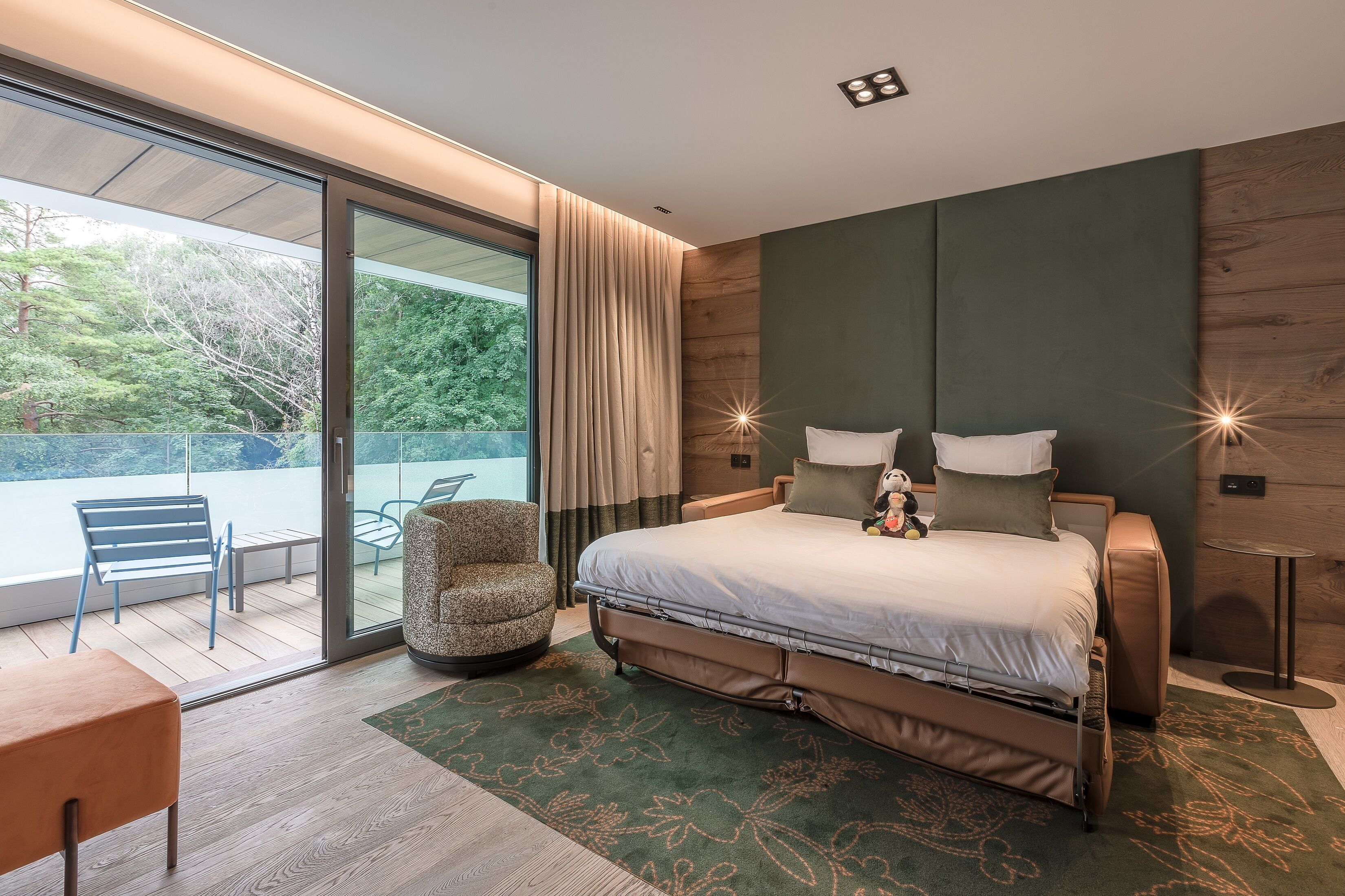 A modern bedroom with a large bed, a seating area with a chair and table, and a view of the outdoors.