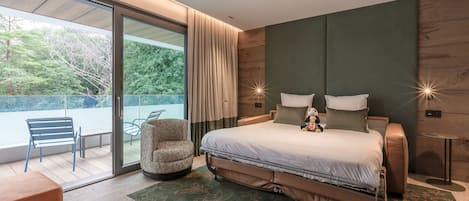 Une chambre moderne avec un grand lit, un coin salon comprenant une chaise et une table, et une vue sur l’extérieur.