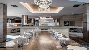 Une cuisine moderne dotée d’un îlot central, d’un coin repas avec une longue table dressée pour le repas, et d’un luminaire sphérique original placé au-dessus de l’îlot.