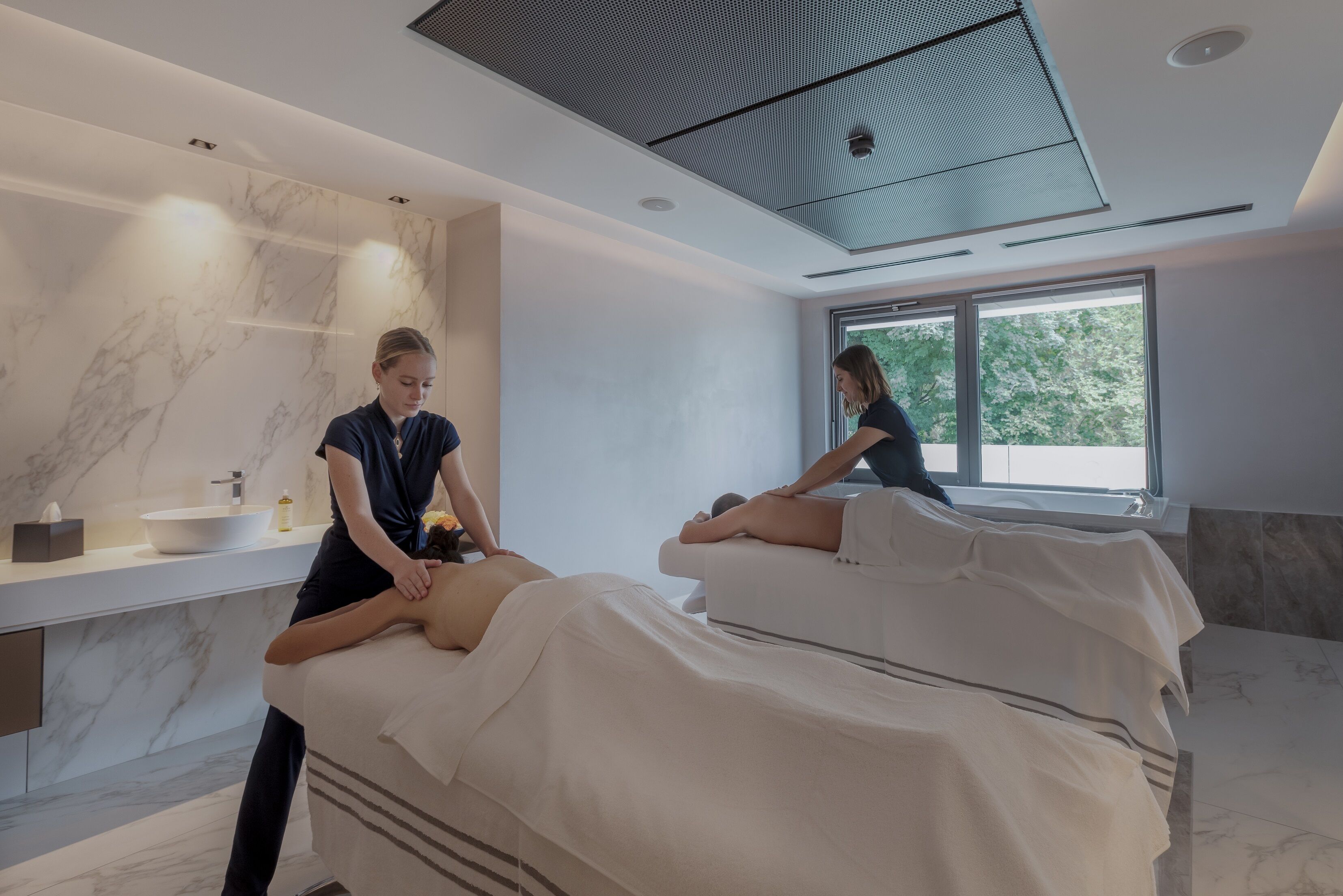 Un spa moderno con dos camillas de masaje, un ventanal grande y una pared de mármol.