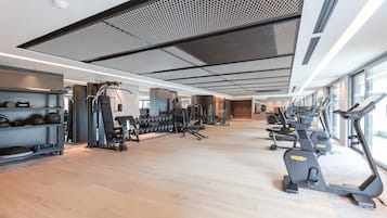 A modern gym with cardio equipment, weight machines, and a wooden floor.