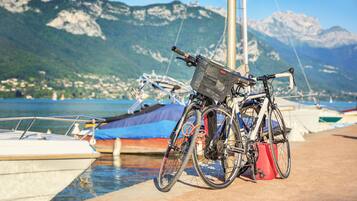 Una bicicleta estacionada cerca de un muelle con barcos y montañas al fondo.