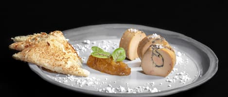 A plate with a piece of toasted bread, a rolled meat dish, and a small meat slice garnished with green leaves.