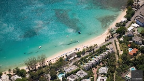 An aerial view of a coastal resort with a beach, clear turquoise waters, and a row of villas. - Tradewinds, villa with sea views & pool, 1min walk to beach.  (Saint Peter)