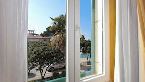 Una ventana con vistas a una calle, palmeras y un edificio con tejado de baldosas.