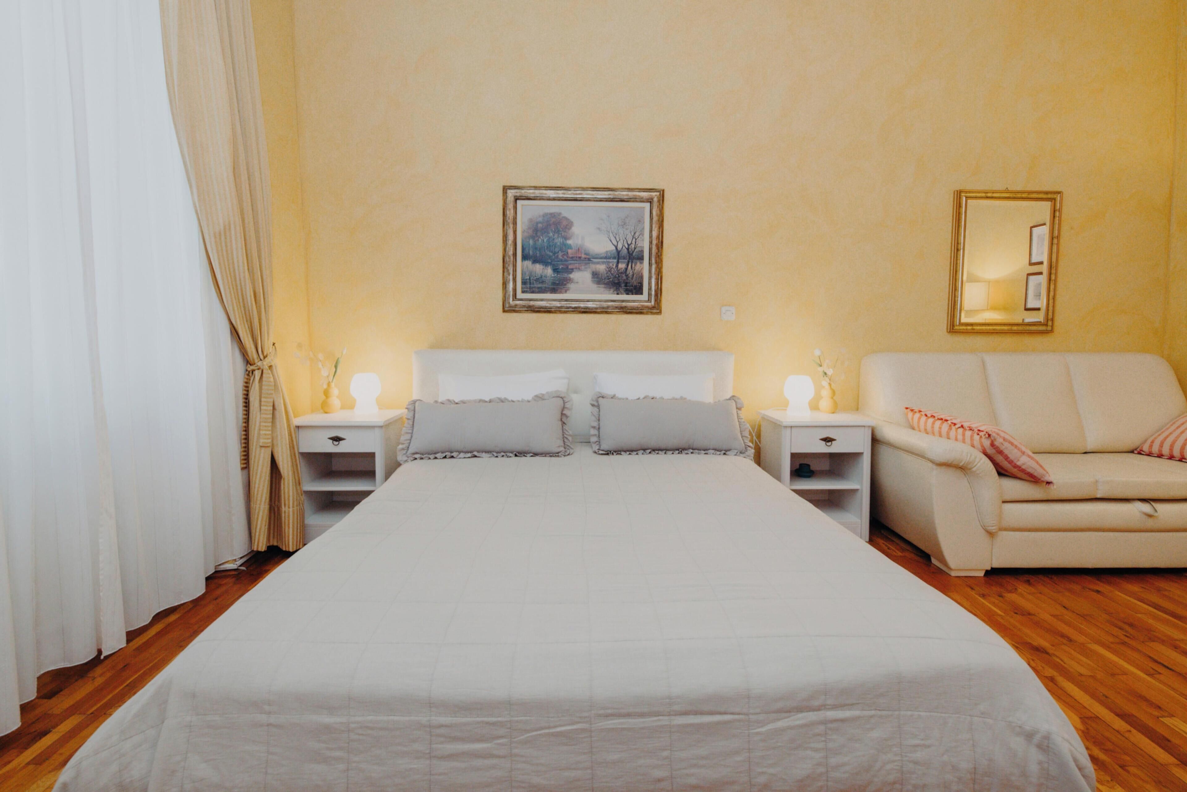 Une chambre à coucher avec un grand lit, deux tables de chevet, une commode, un canapé et un tableau au mur.