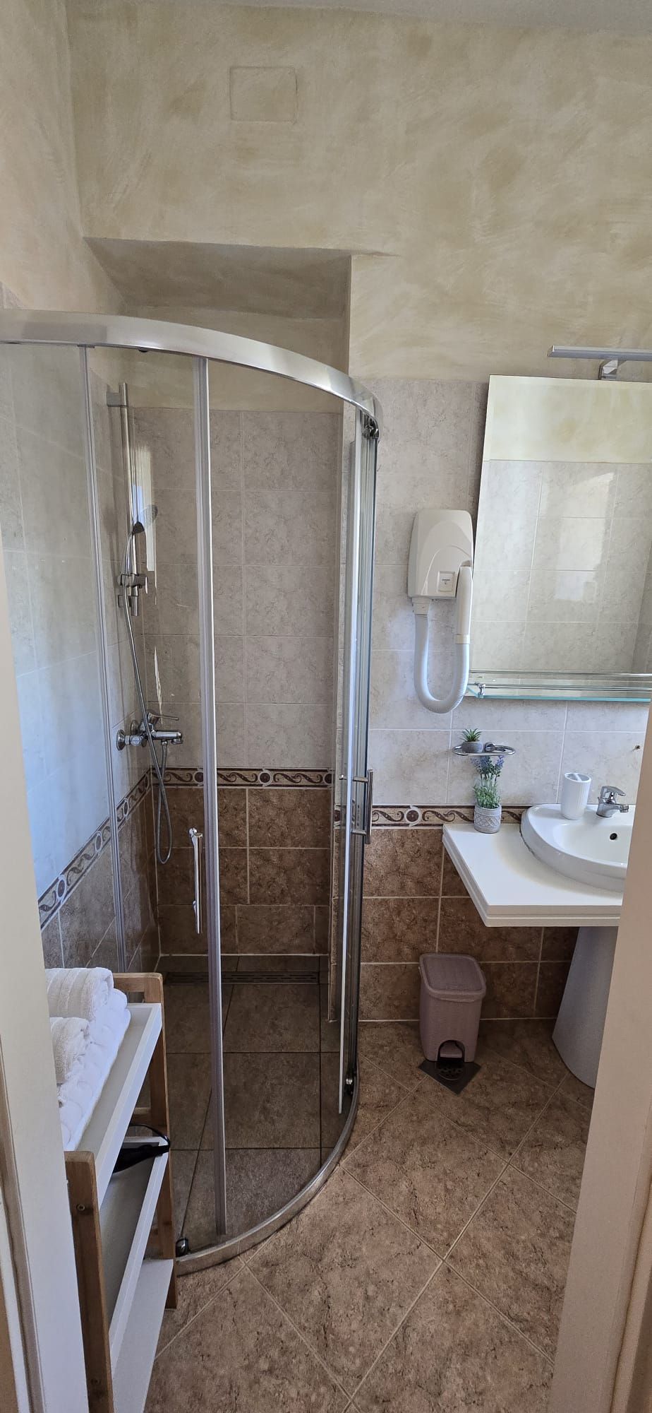 A bathroom with a glass shower enclosure, a sink, and a mirror.