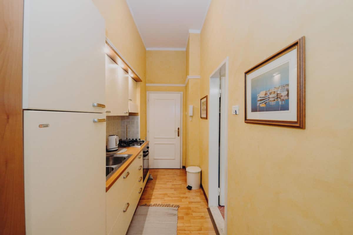 Un couloir étroit avec un coin cuisine d’un côté, une porte au fond et un tableau encadré au mur.