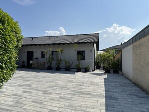 Um edifício moderno com telhado em azulejos, plantas em vasos e um pátio pavimentado.
