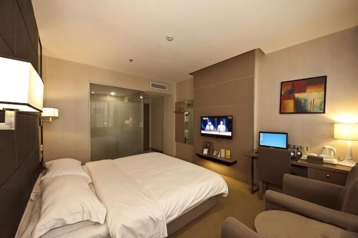 Ein Hotelzimmer mit Bett, Fernseher, Schreibtisch und Computer sowie einem Sessel.